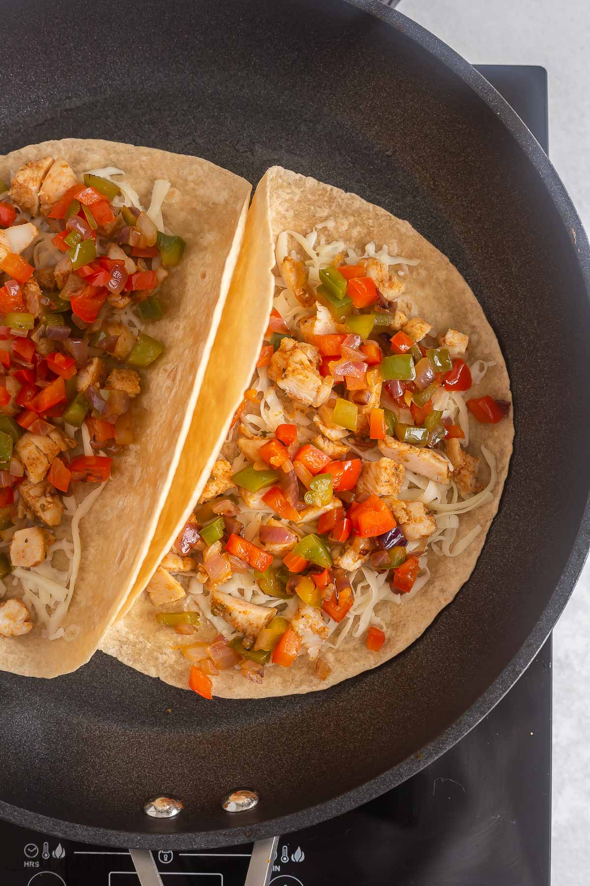 cheese peppers and chicken in a tortilla in skillet.