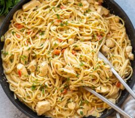 overhead image of chicken spaghetti in black skillet with tongs.
