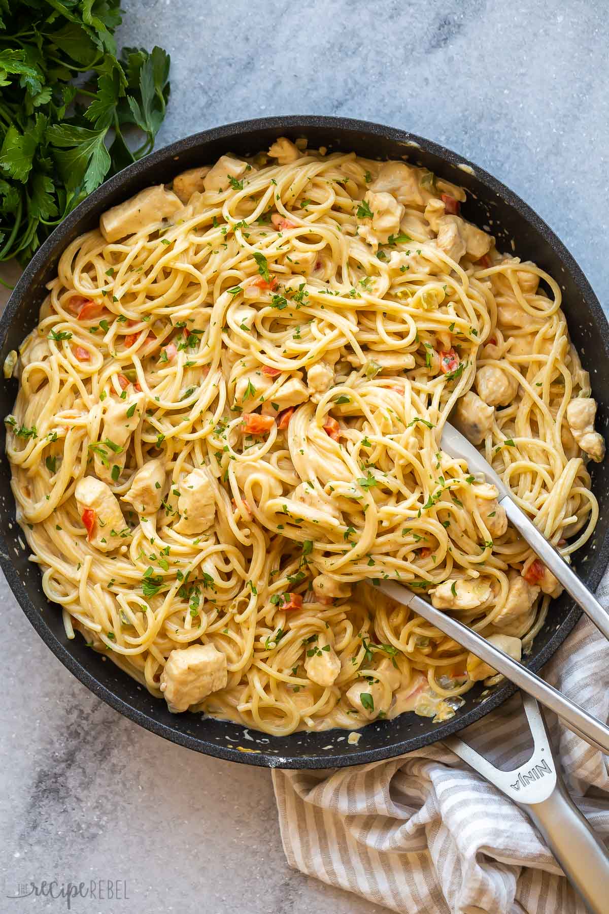 overhead image of chicken spaghetti in black skillet with tongs.