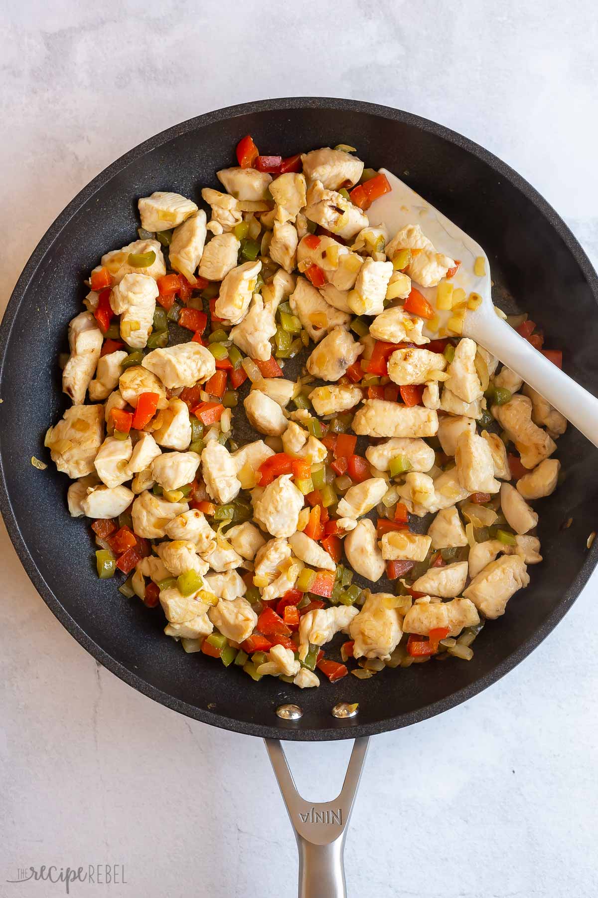 chicken added to peppers in black skillet.