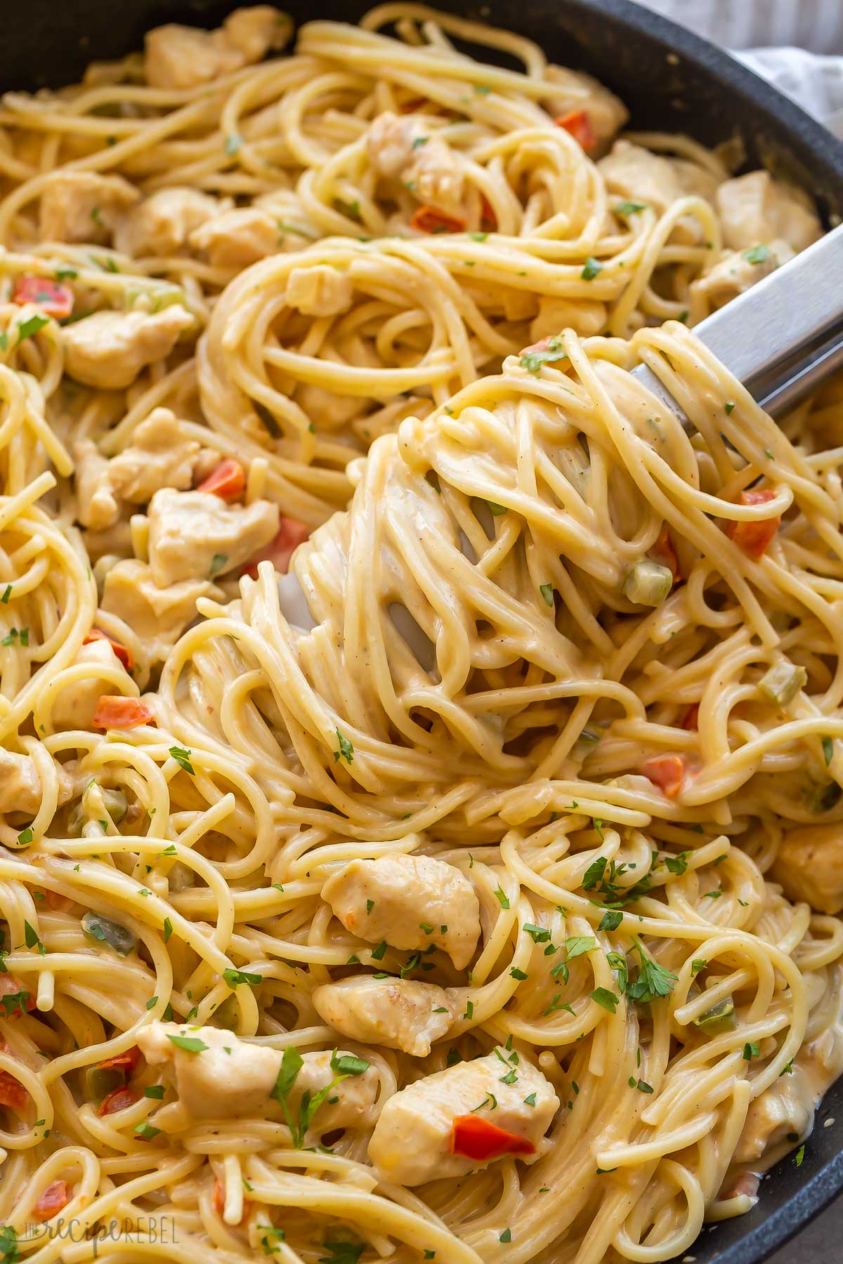 close up image of spaghetti twirled around tongs in pan.
