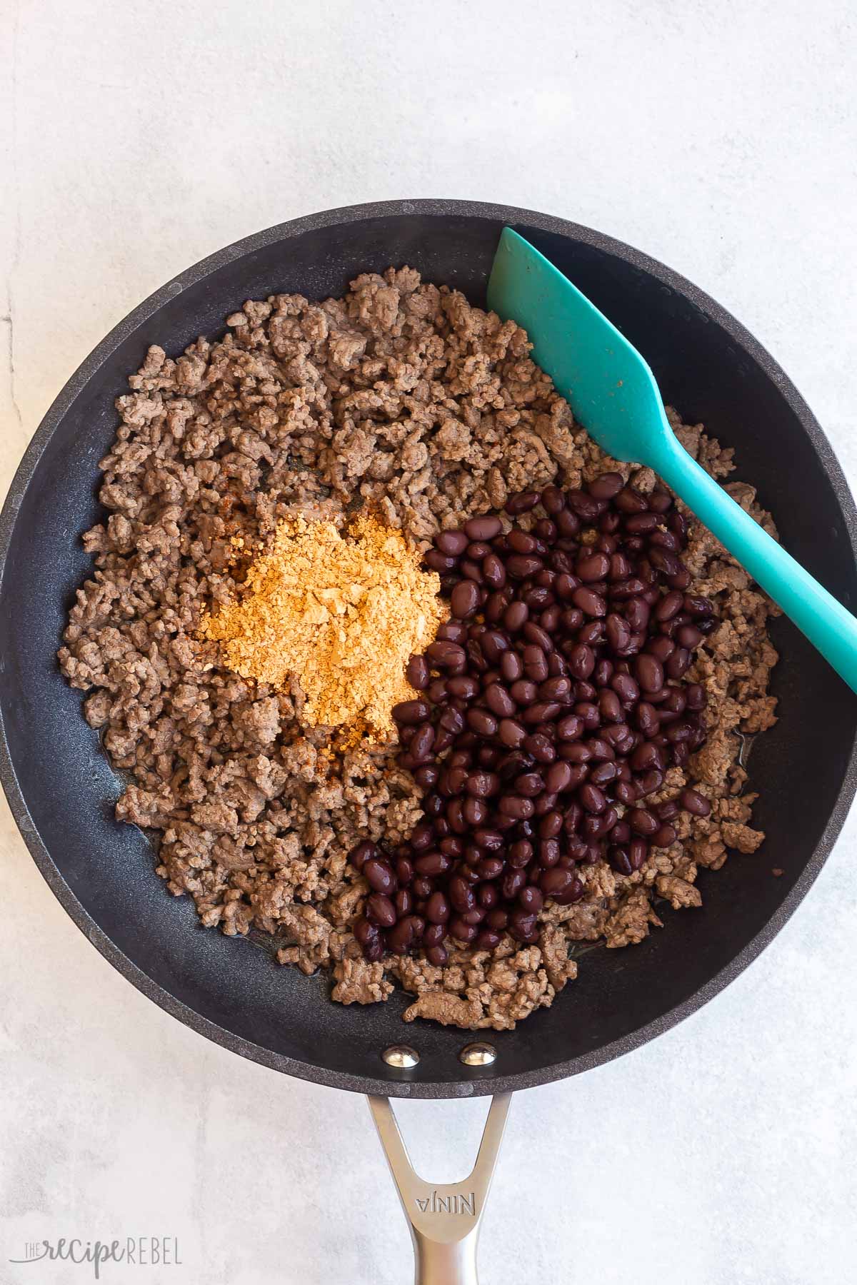 taco seasoning and beans added to cooked ground beef in skillet