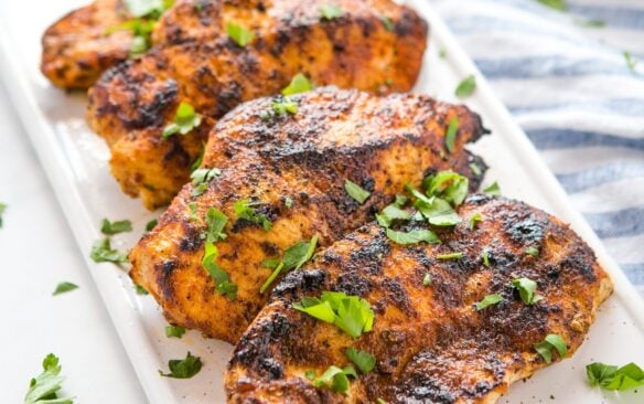 white plate with cajun grilled chicken breasts garnished with herbs