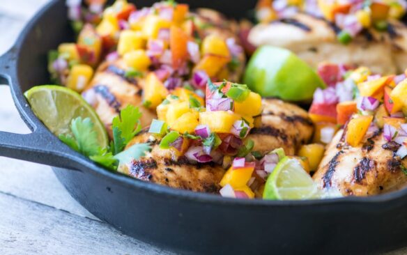 cast iron skillet with grilled chicken breasts topped with peach salsa.