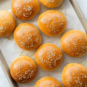 golden burger buns on a baking sheet with parchment paper