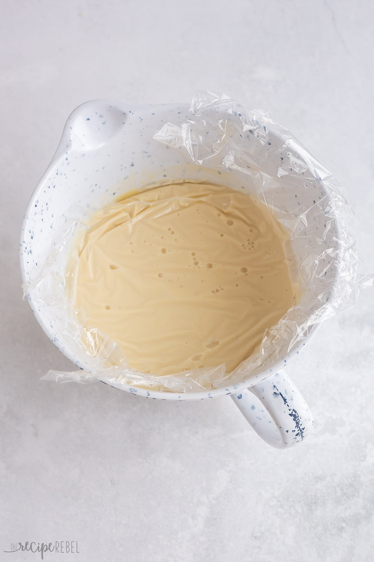 ice cream base in white bowl with plastic wrap pressed to the top.
