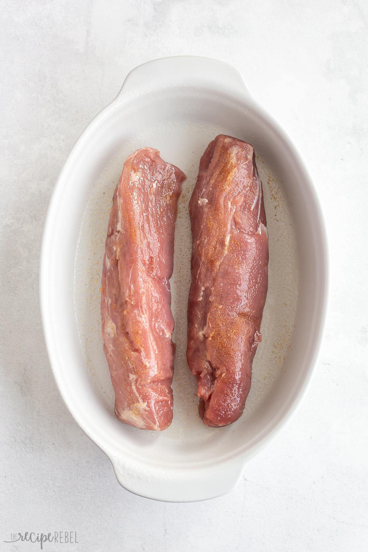 two pork tenderloins in a white baking dish with no sauce