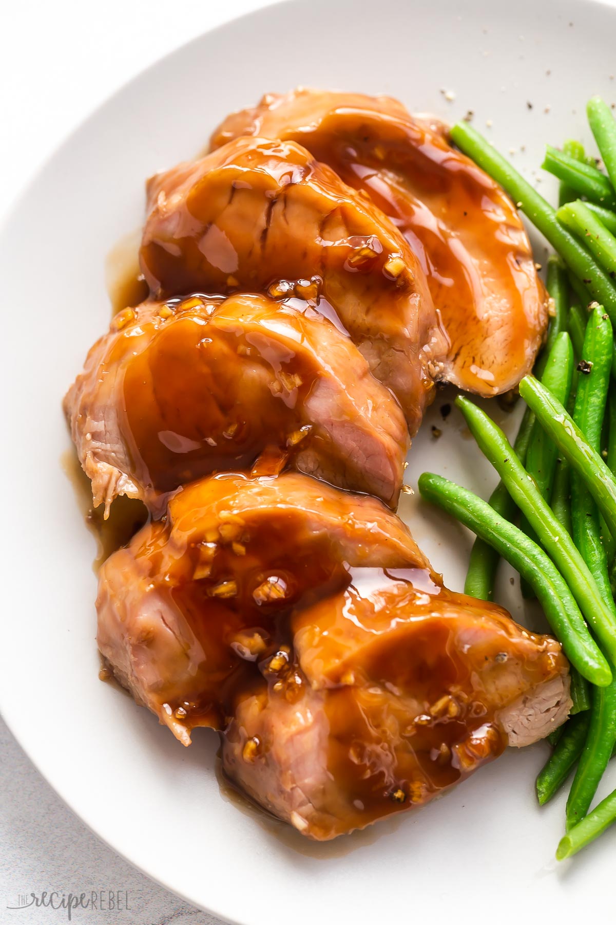 close up image of five slices of pork tenderloin on plate with green beans