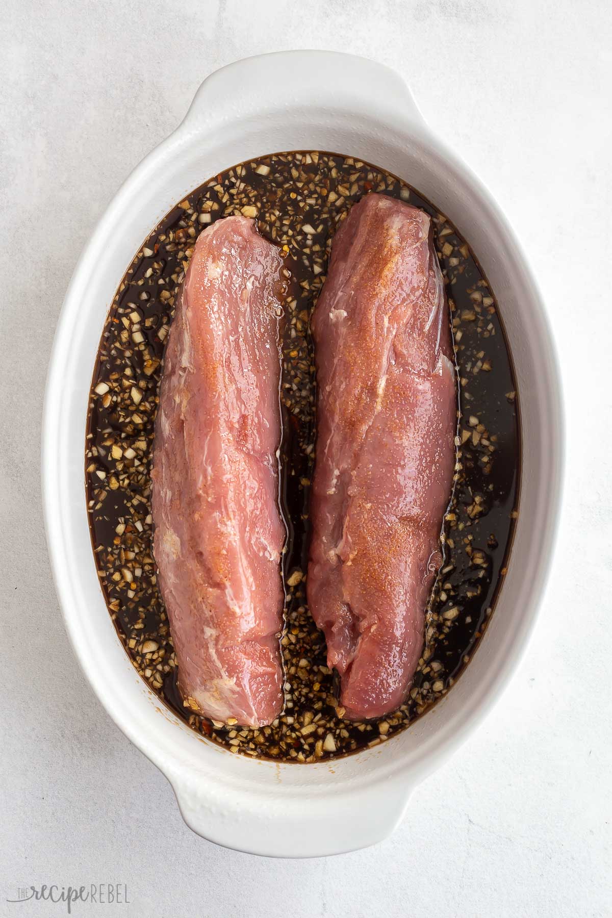 two pork tenderloins in white baking dish with sauce on the bottom