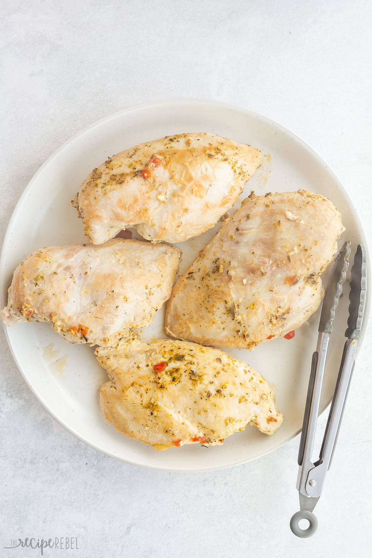 cooked chicken breasts removed to a white plate with tongs on the side