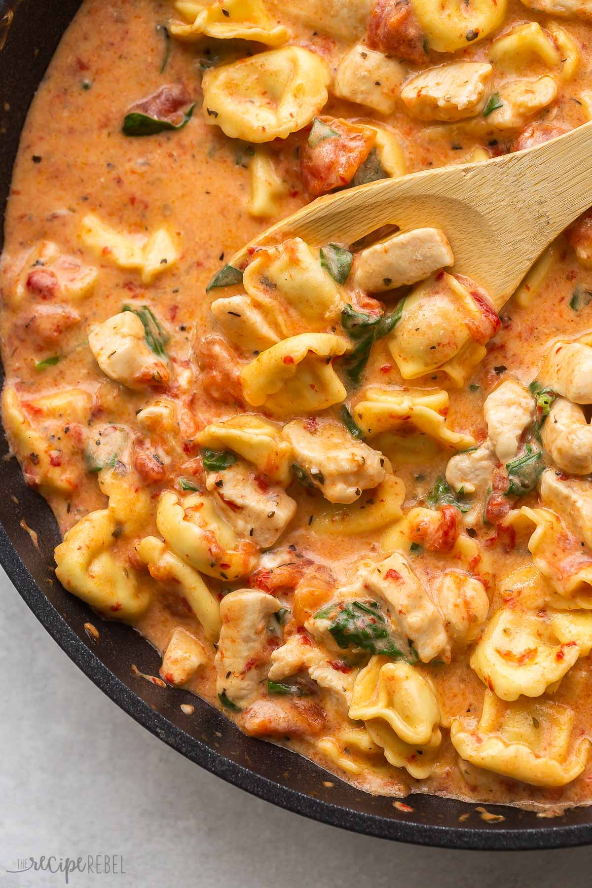 close up image of italian chicken tortellini with wooden spoon scooping.