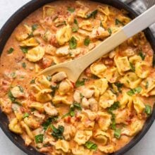 large black skillet of italian tortellini with wooden spoon stuck in.