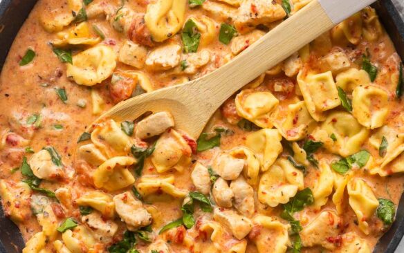 large black skillet of italian tortellini with wooden spoon stuck in.