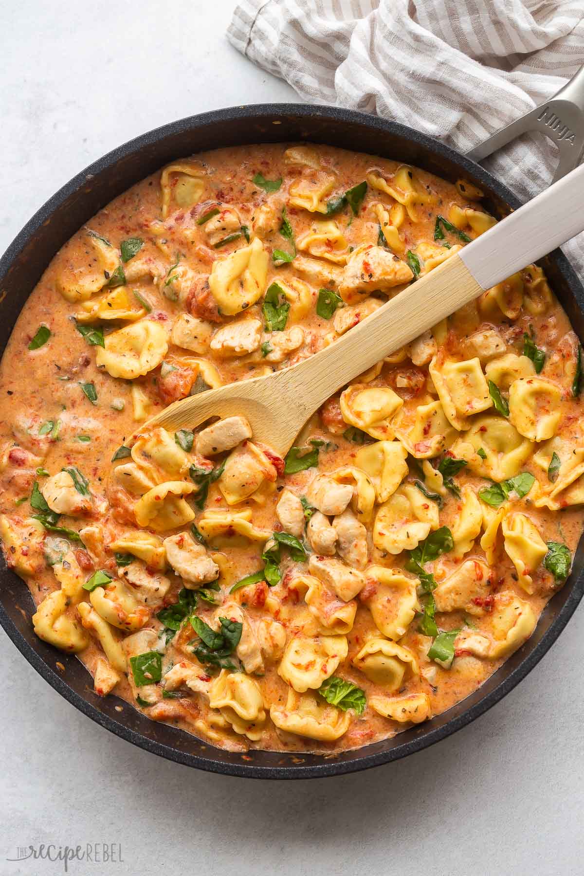 large black skillet of italian tortellini with wooden spoon stuck in.