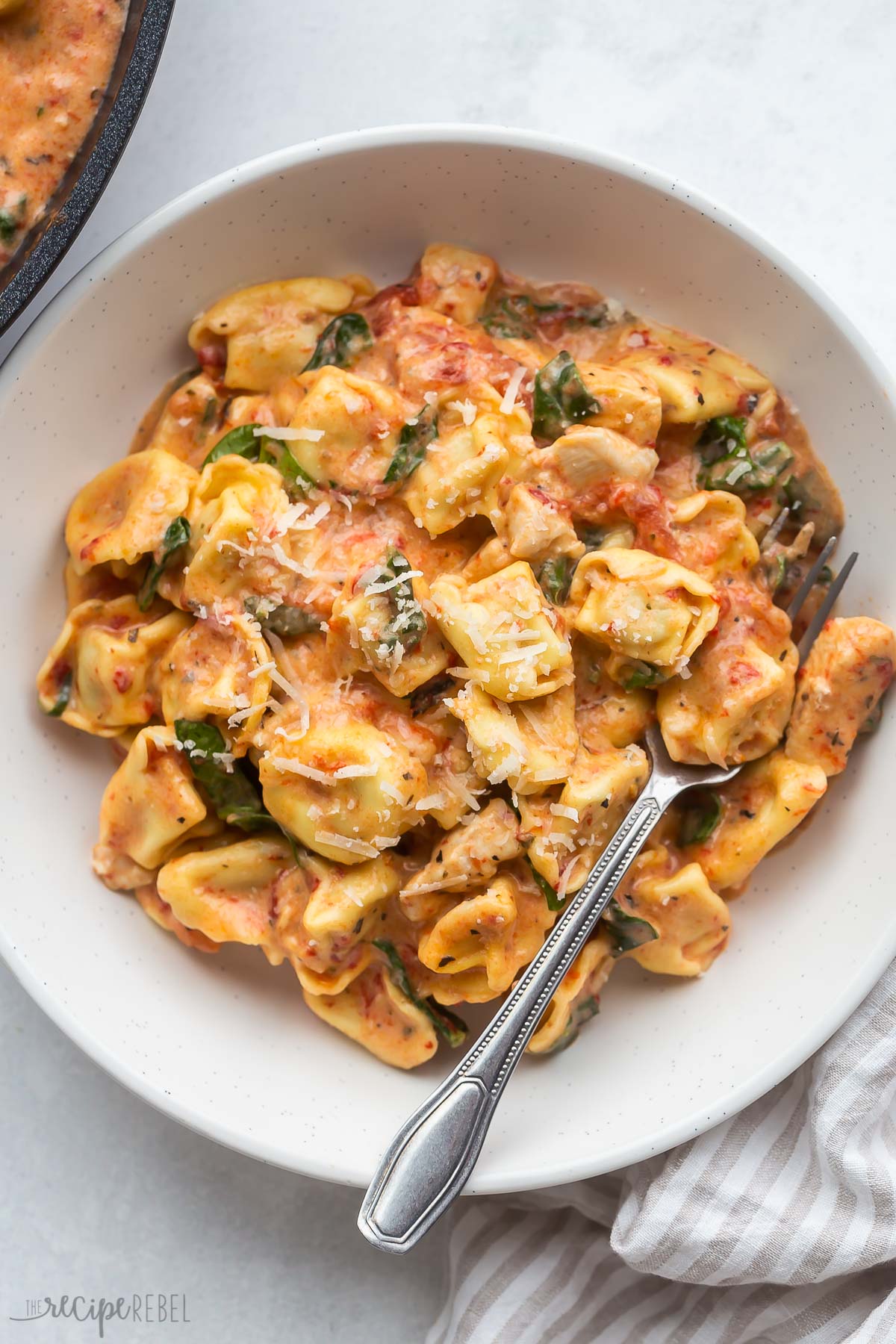 italian chicken tortellini in beige bowl with parmesan sprinkled on top.