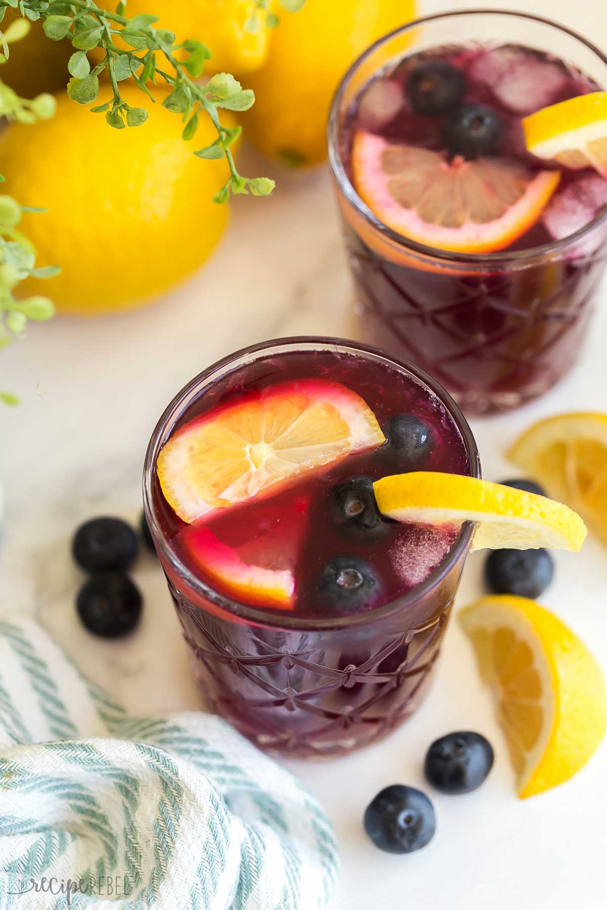 two glasses of blueberry lemonade with lemon wedges and blueberries
