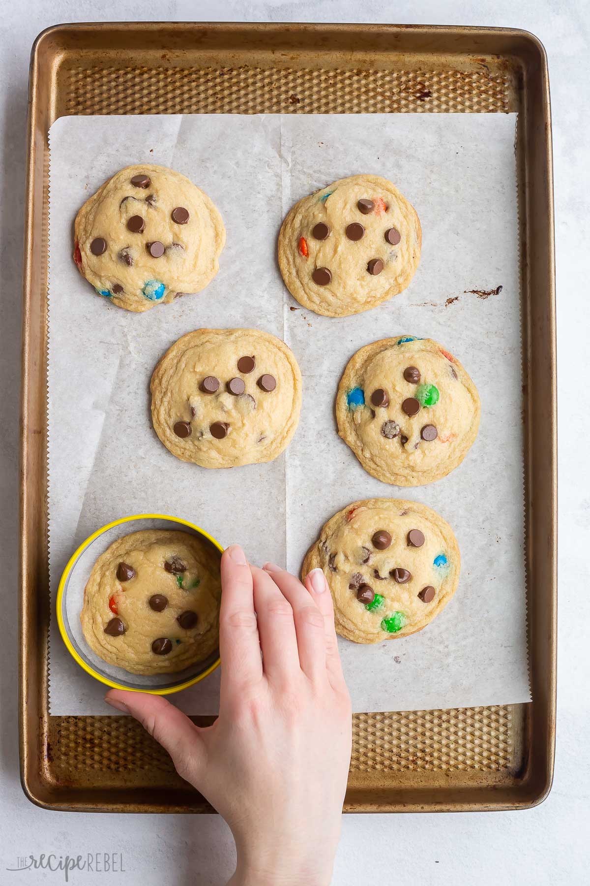 round cookie cutter reshaping warm baked cookies on pan.