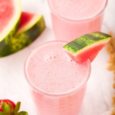 two glasses of watermelon smoothie with watermelon wedge on the side.