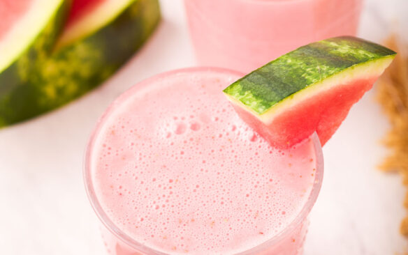 two glasses of watermelon smoothie with watermelon wedge on the side.