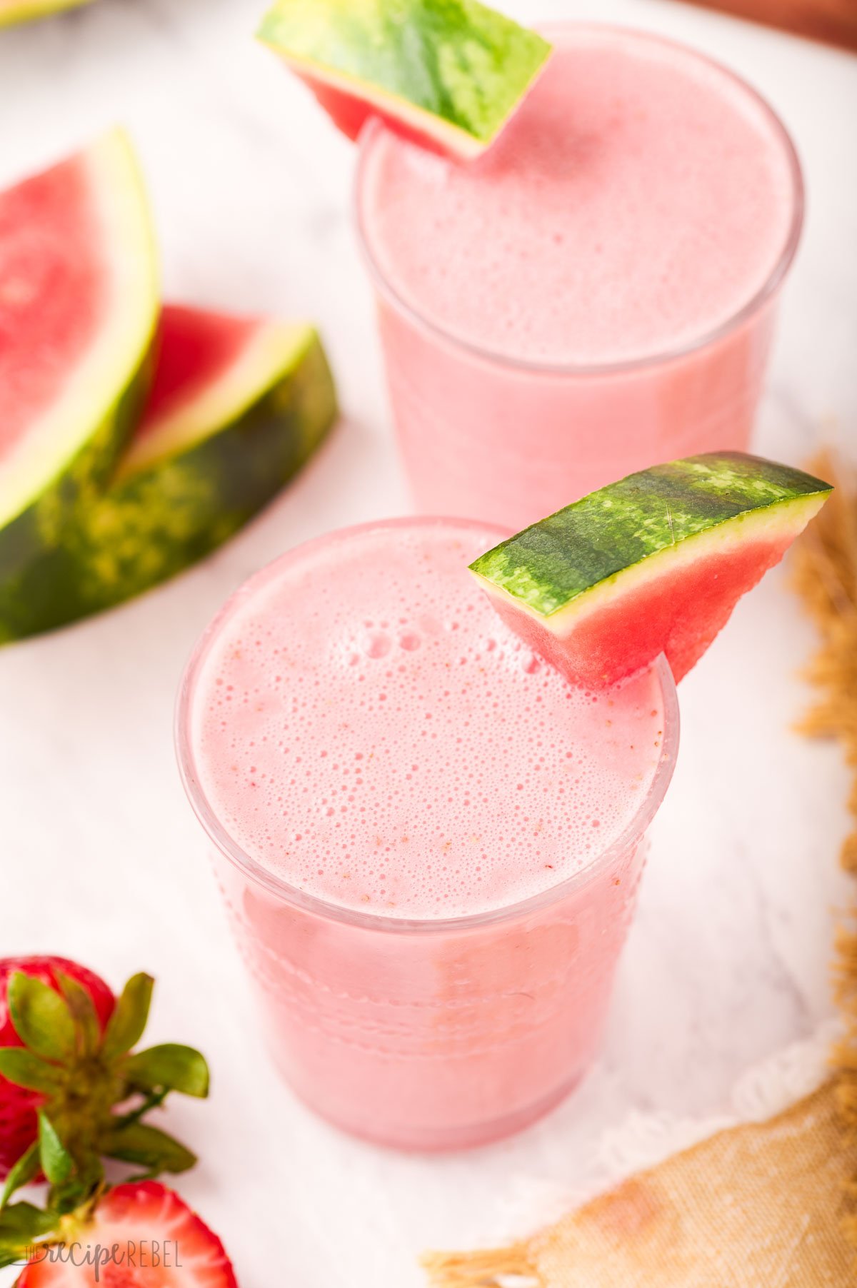 two glasses of watermelon smoothie with watermelon wedge on the side.