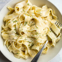 tagliatelle pasta in feta sauce with fresh dill and fork stuck in noodles.