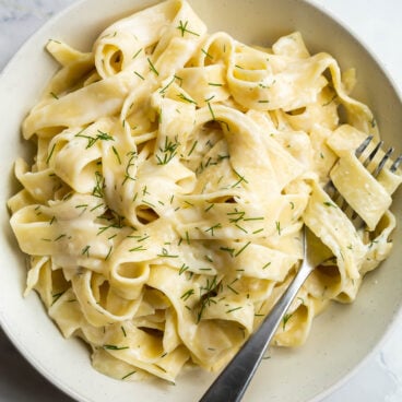 tagliatelle pasta in feta sauce with fresh dill and fork stuck in noodles.