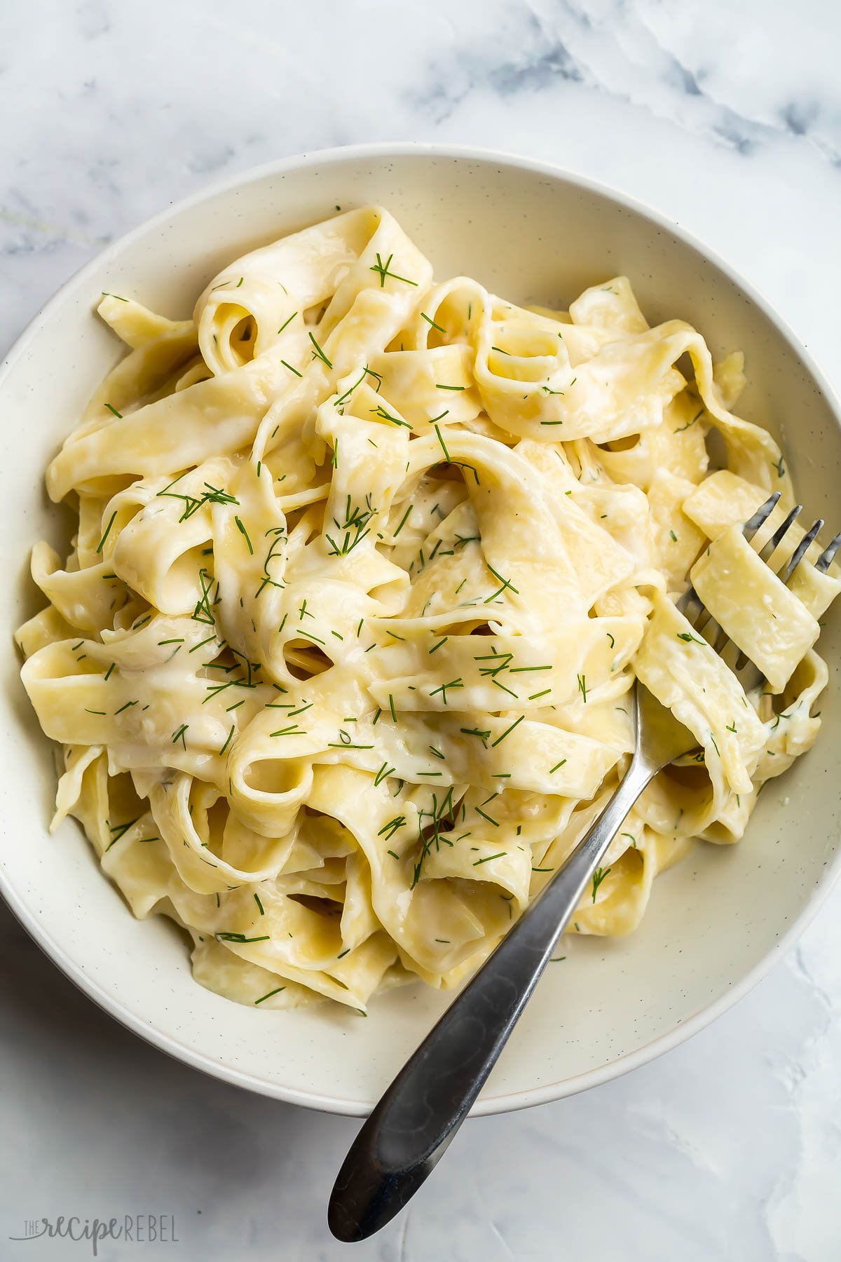 tagliatelle pasta in feta sauce with fresh dill and fork stuck in noodles.