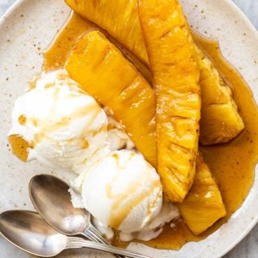 three slices of grilled pineapple on a plate with vanilla ice cream.