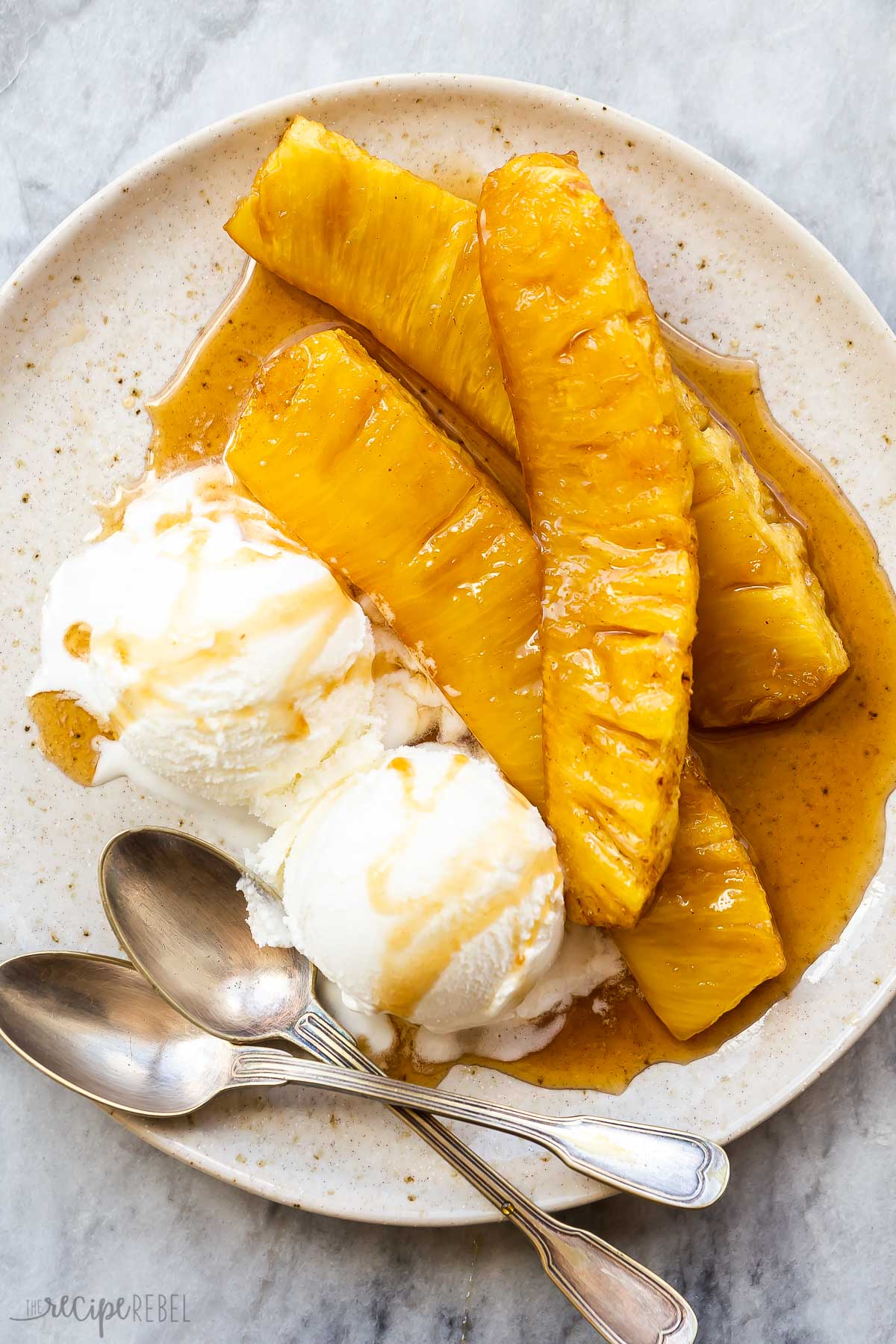 three slices of grilled pineapple on a plate with vanilla ice cream.