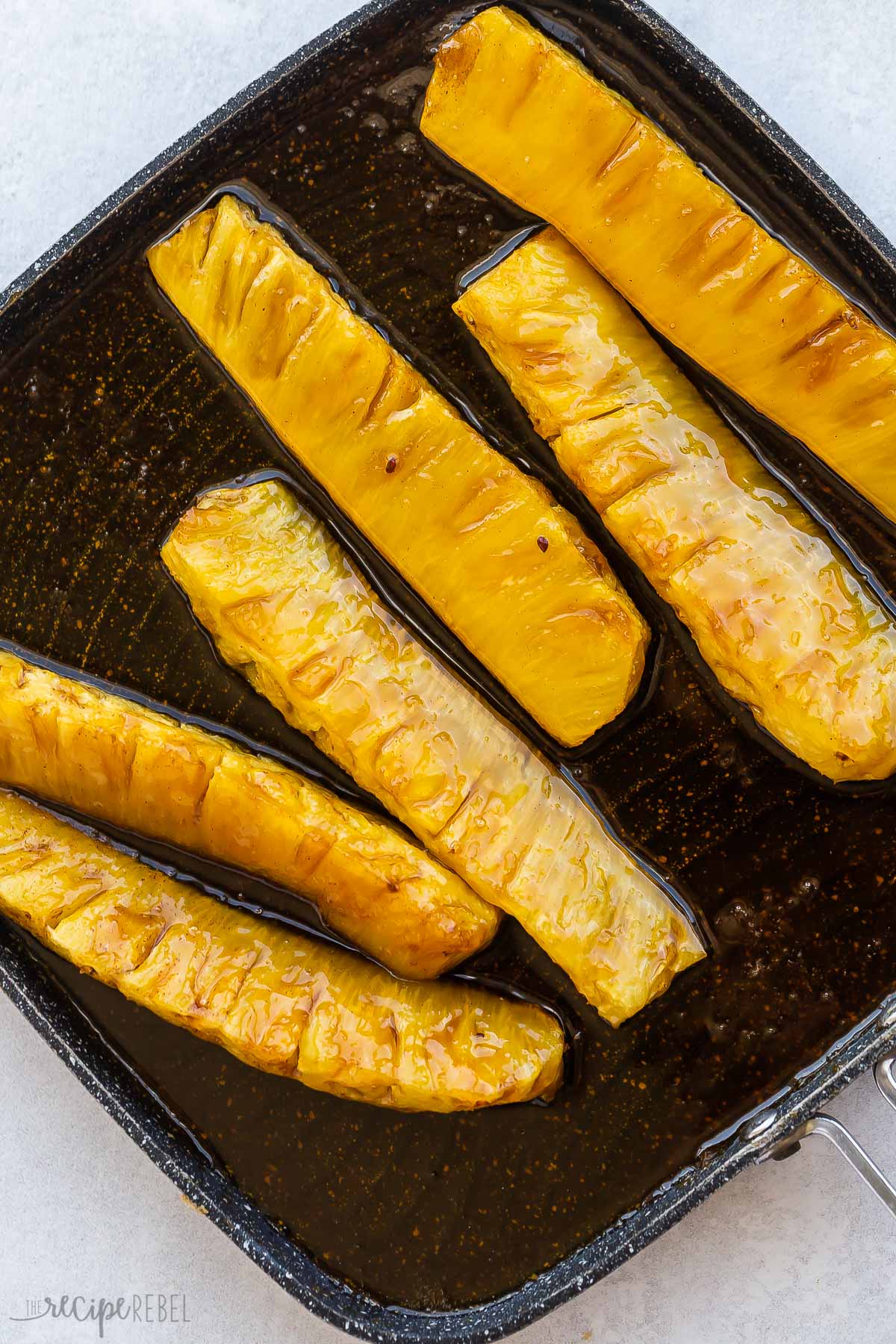 six pineapple spears on black grill pan.