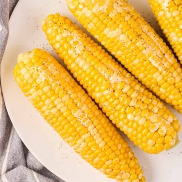 overhead image of four cobs of corn on white plate.