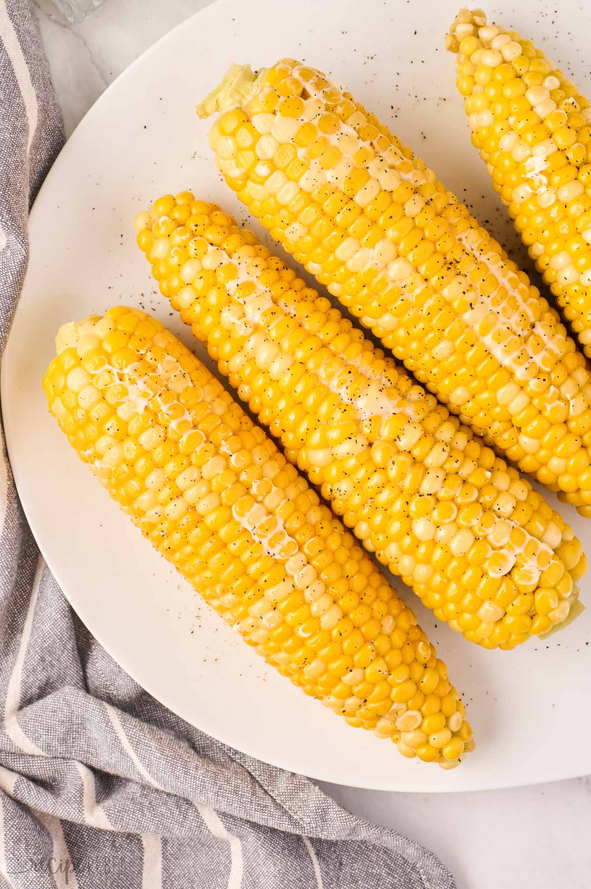 overhead image of four cobs of corn on white plate.