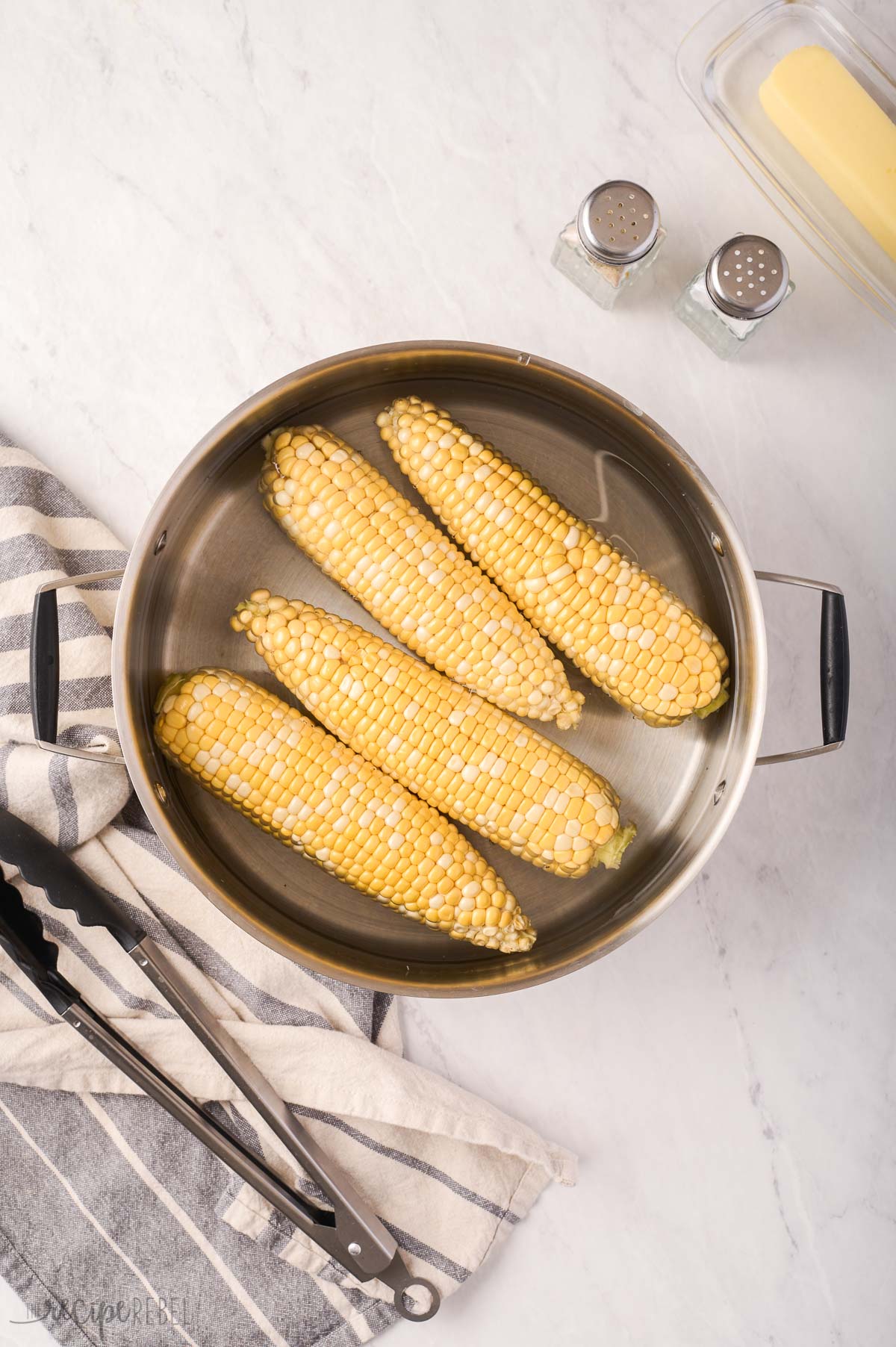 uncooked cobs of corn in pot of water.