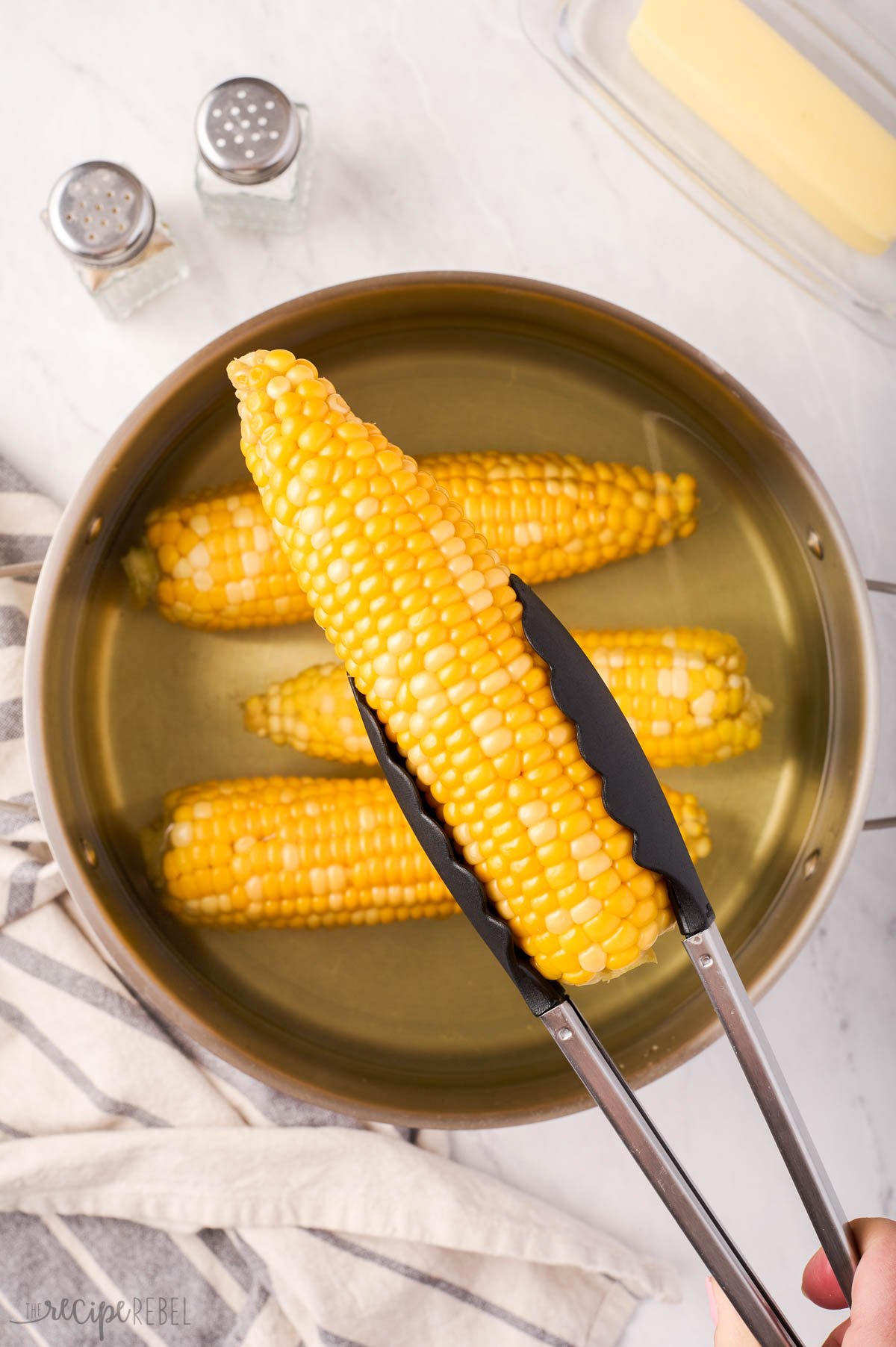 tong holding boiled corn on the cob.