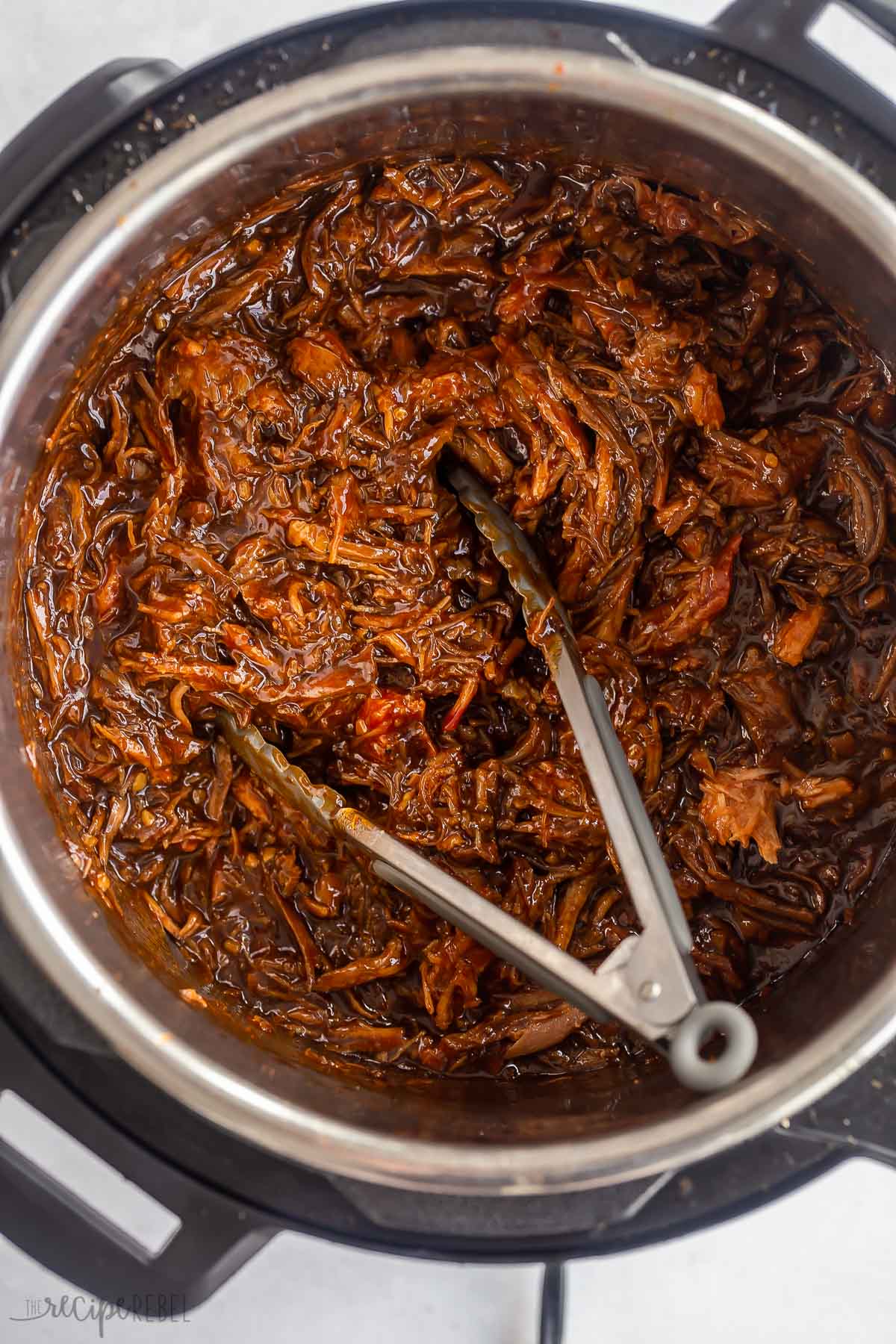 overhead image of instant pot pulled pork in pressure cooker with tongs.