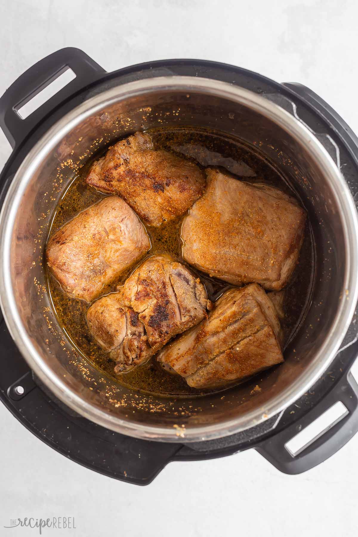 chunks of seared pork shoulder in instant pot with liquid.