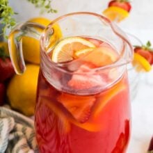 pitcher of strawberry lemonade with ice cubes lemon slices and sliced strawberries.