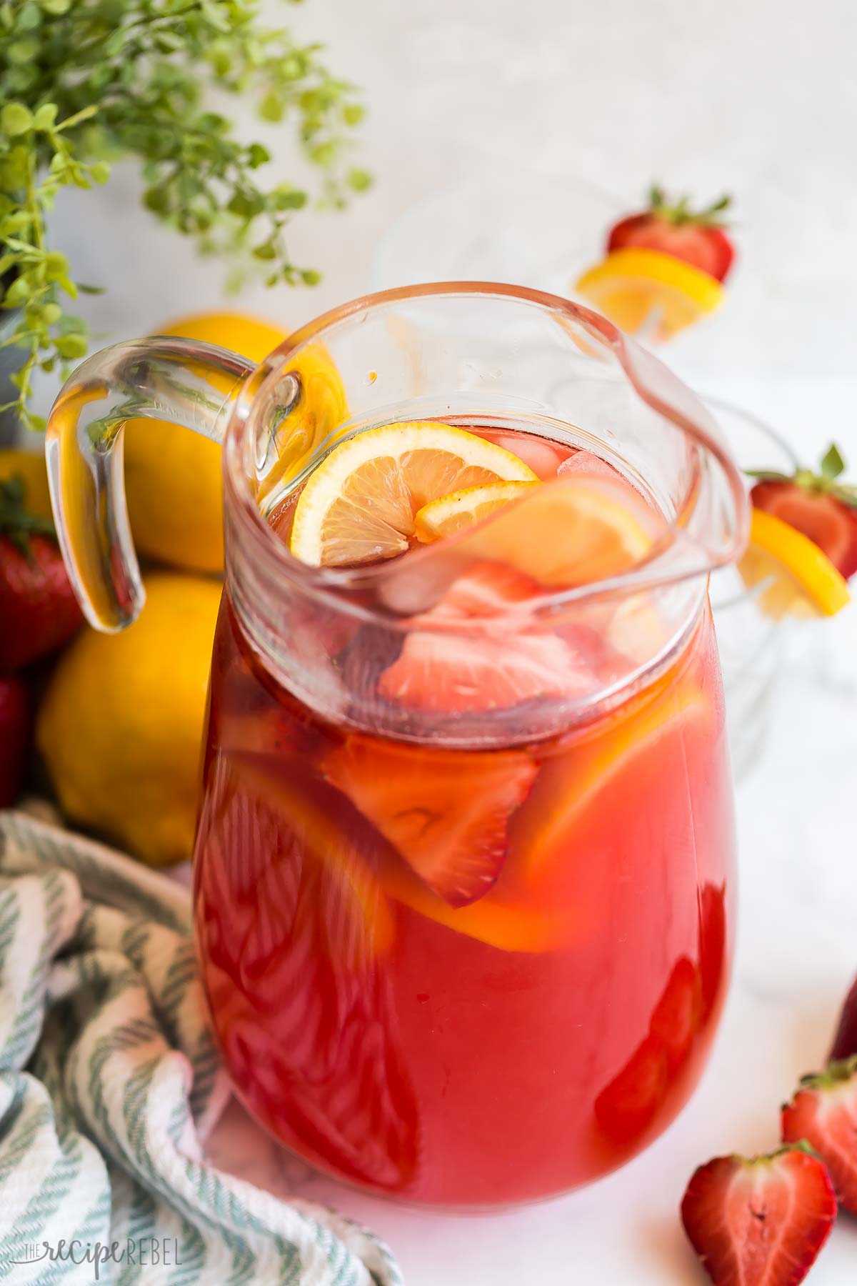 pitcher of strawberry lemonade with ice cubes lemon slices and sliced strawberries.