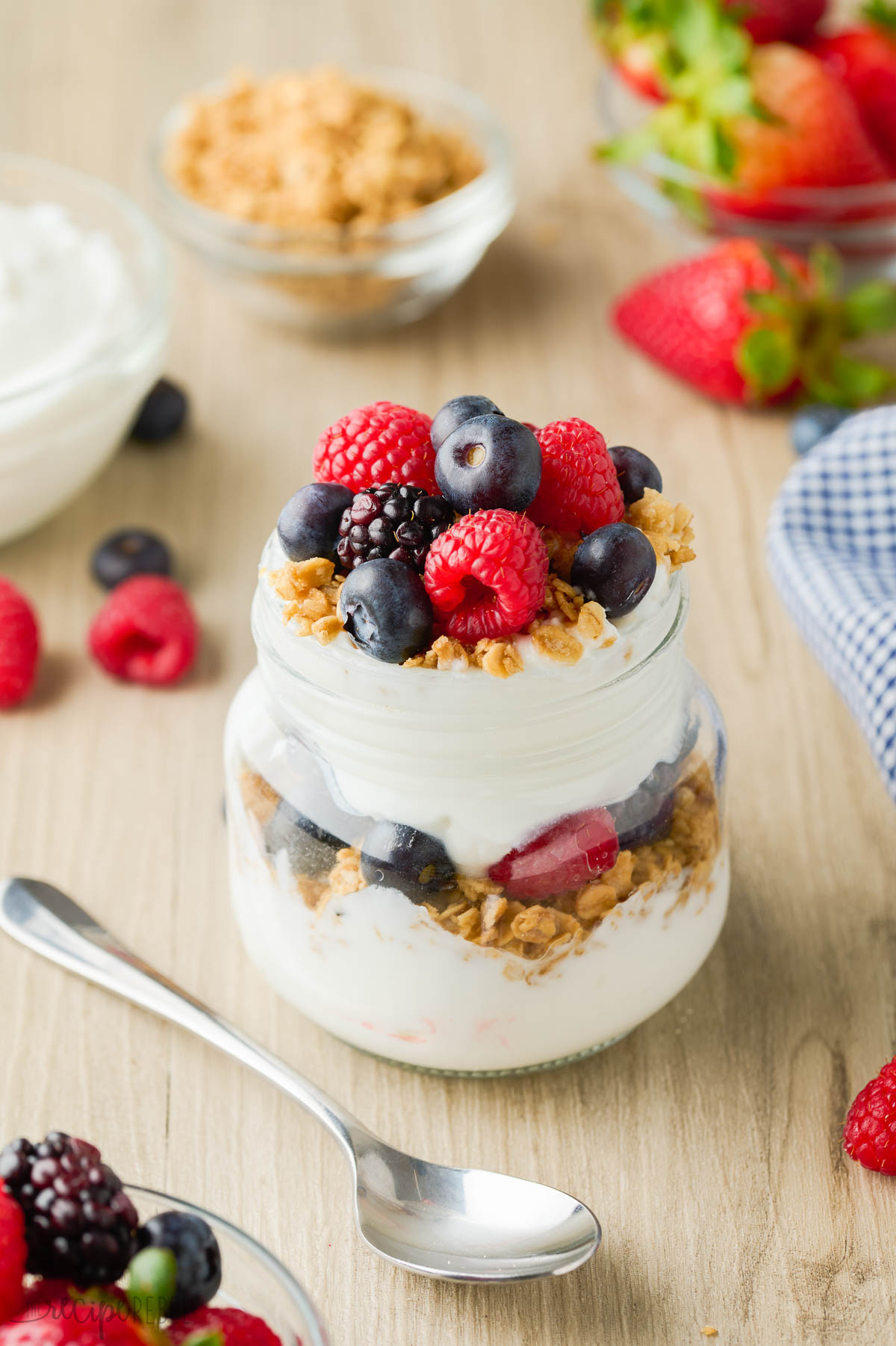 yogurt parfait with vanilla yogurt granola and berries in small glass jar.