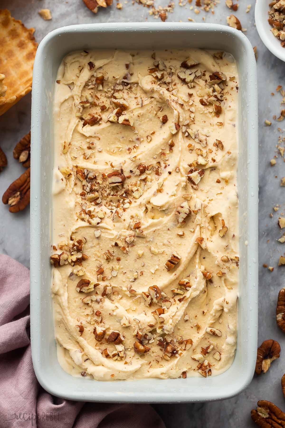 overhead image of butter pecan ice cream in a blue loaf pan with nuts on top.