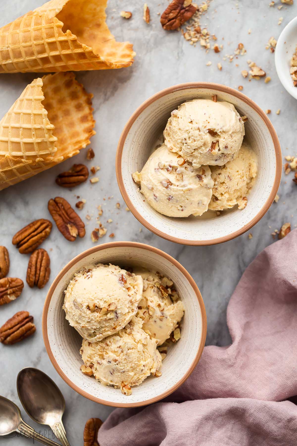 two bowls of homemade ice cream with pecans and cones all around.