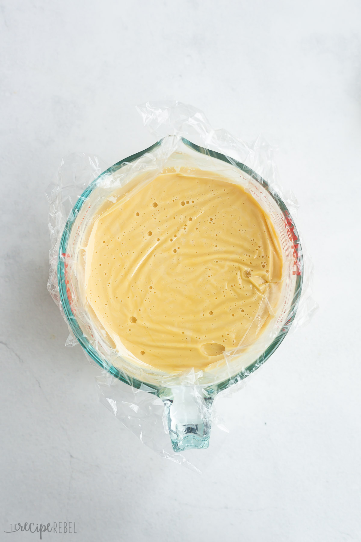 custard in a glass measuring cup with plastic wrap on top to chill.
