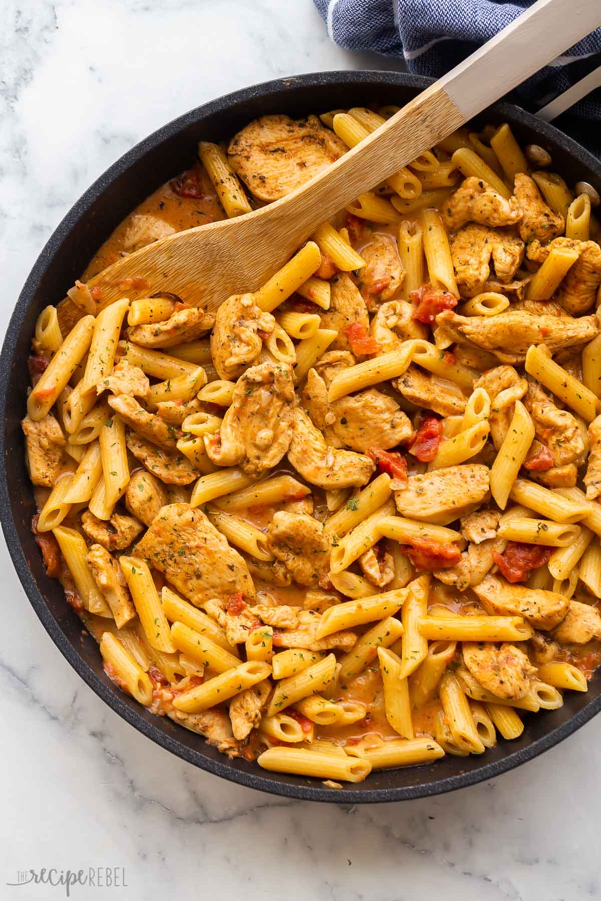 skillet of cajun chicken penne pasta with wooden spoon.