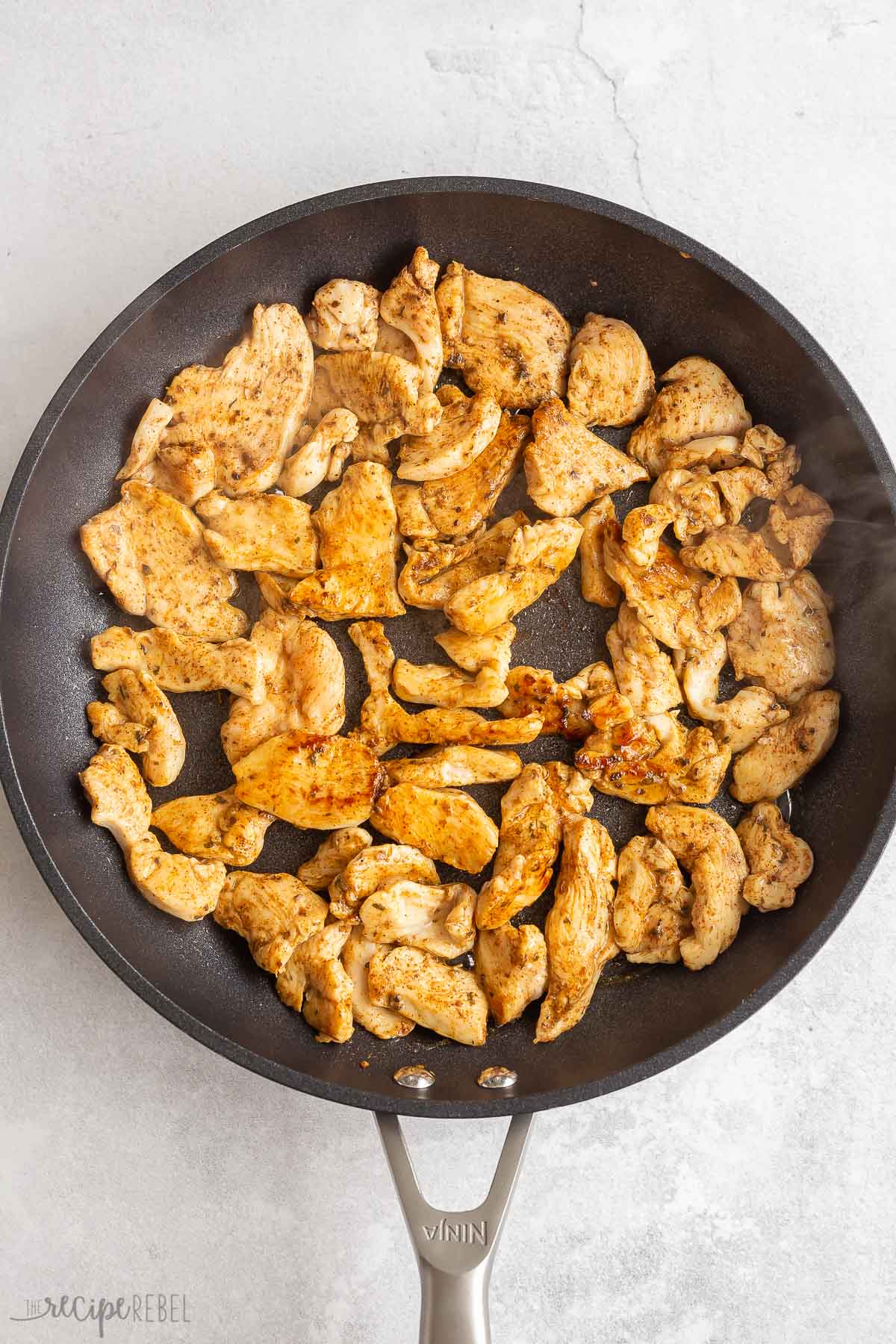 sliced seasoned chicken cooking in black skillet.