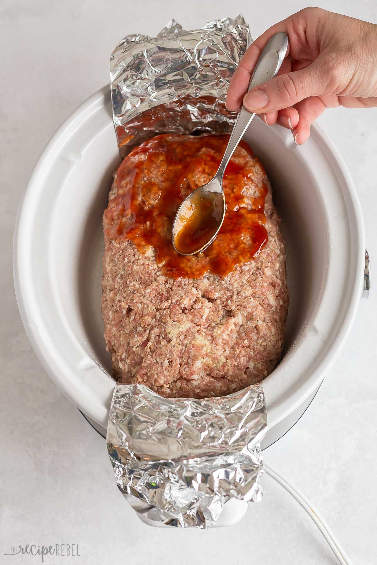 glaze being spread on uncooked crockpot meatloaf.
