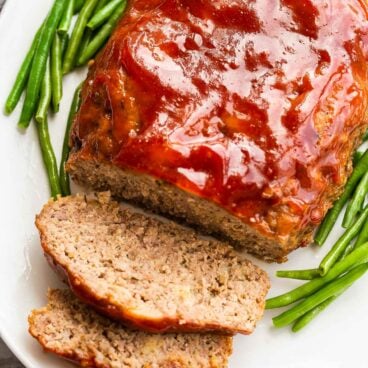 crockpot meatloaf on white platter with green beans.