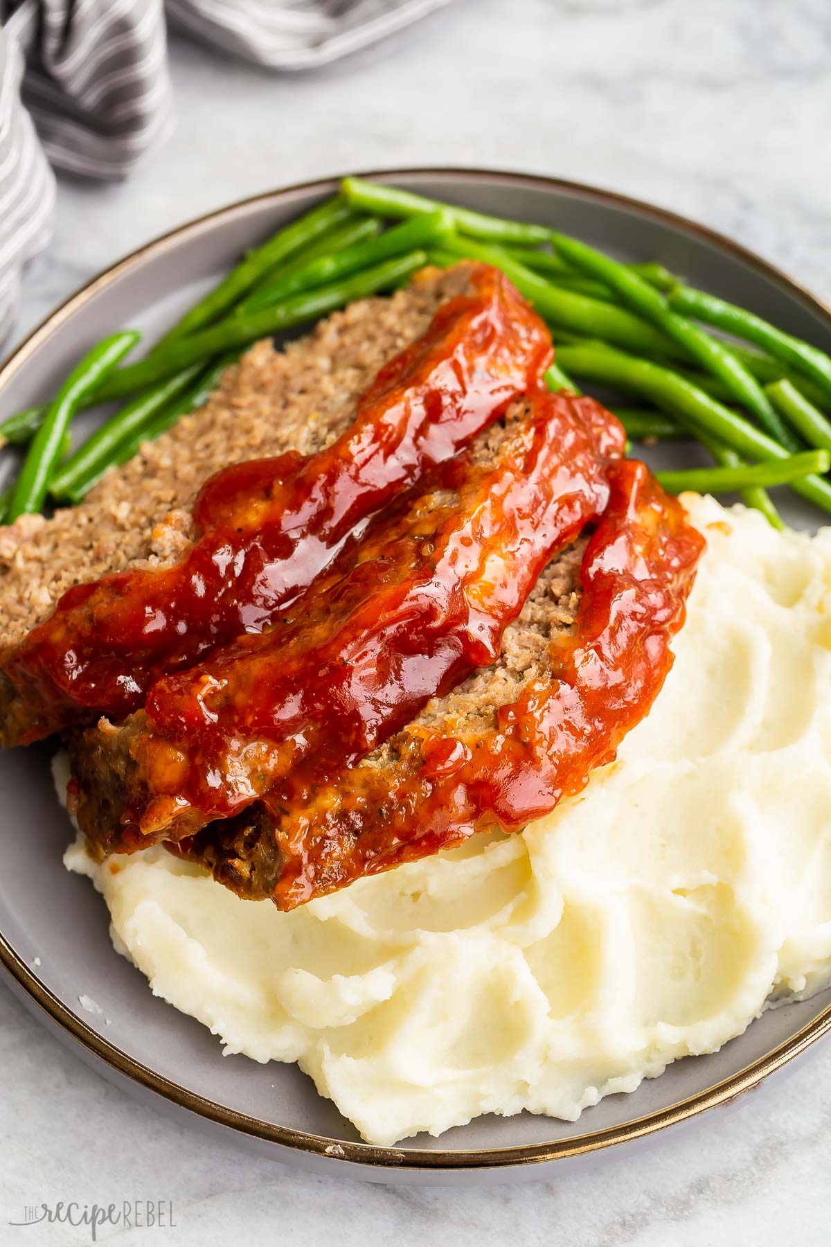 close up image of three slices of meatloaf with mashed potatoes and green beans.