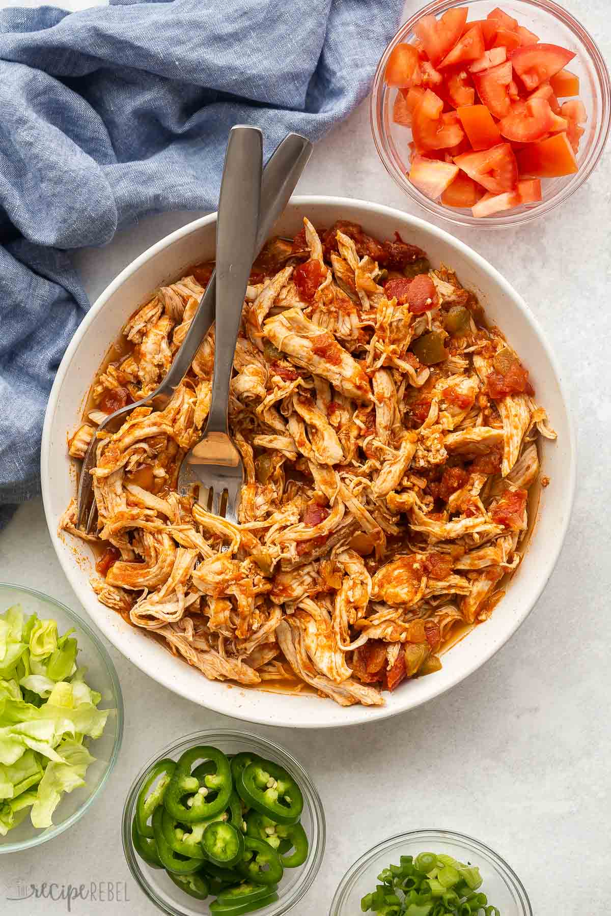 bowl of salsa chicken with two forks stuck in and toppings all around.