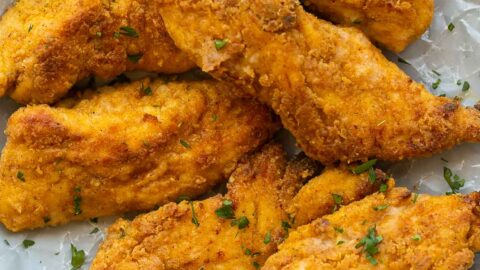 crispy oven fried chicken on a plate lined with parchment paper.