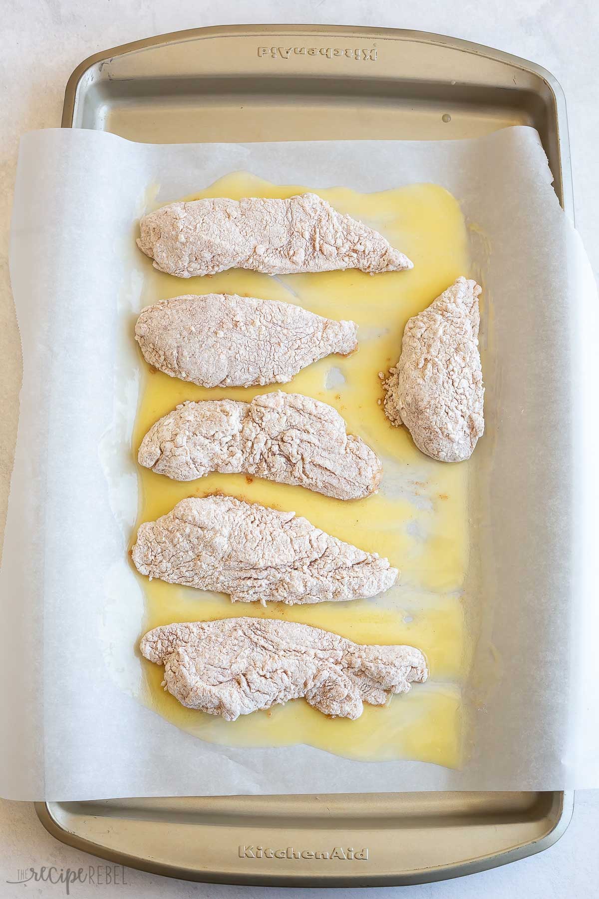 breaded chicken pieces added to baking sheet with parchment paper and melted butter.